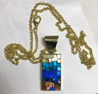 A gold chain with a blue and gold rectangle pendantDescription automatically generated